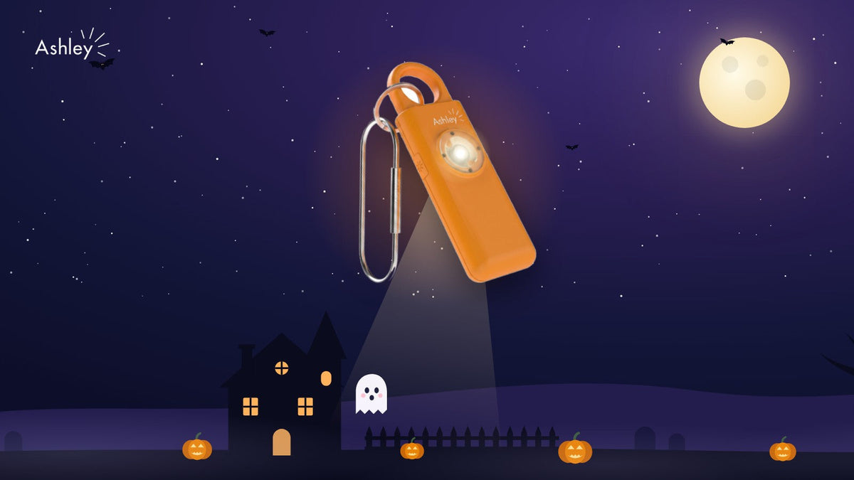 Orange Ashley personal alarm with its torch on under a Halloween moon